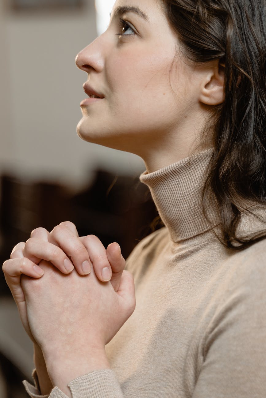 A serene cathedral interior, stained glass windows casting warm, ethereal light. In the foreground, a lone figure kneels in prayer, hands clasped, head bowed. Their face is obscured, but a sense of reverence and supplication is palpable. The middle ground is filled with pews, empty save for a scattering of candles, their flickering flames casting gentle shadows. The background recedes into a hazy, expansive space, the high vaulted ceilings and ornate architecture evoking a profound sense of the sacred. The scene is bathed in a soft, golden glow, creating an atmosphere of solemnity and protection.